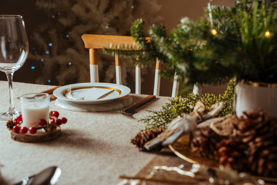 Homely christmas table setting, decorated with pine branches and rustic tablecloth in the living room of home tree lit background