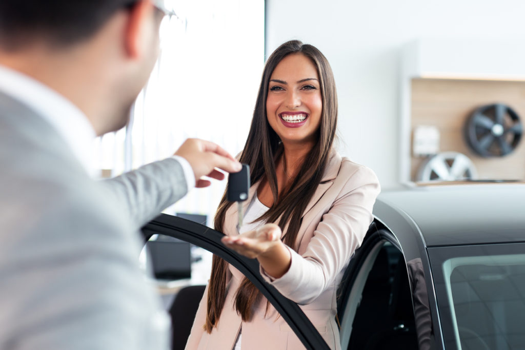 Smiling car salesman handing over your new car keys. Happy girl the buyer.