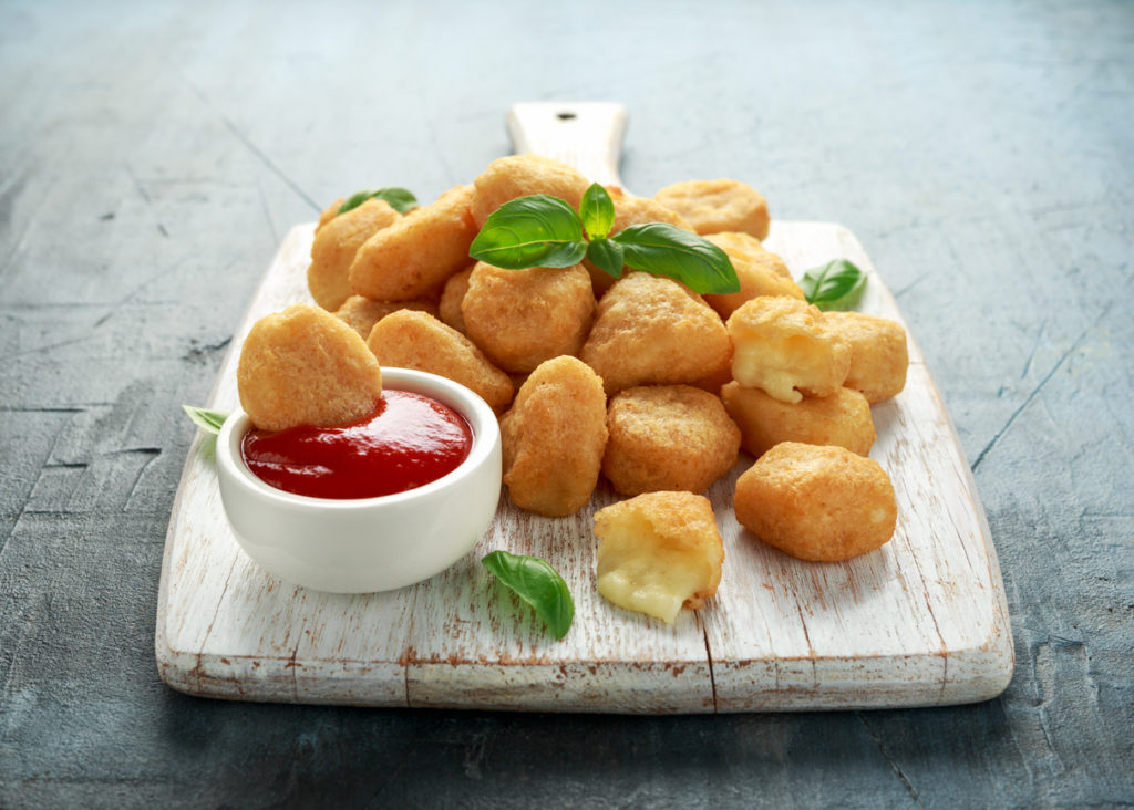 Fried mozzarella, cheddar cheese bites, balls with ketchup on white wooden board