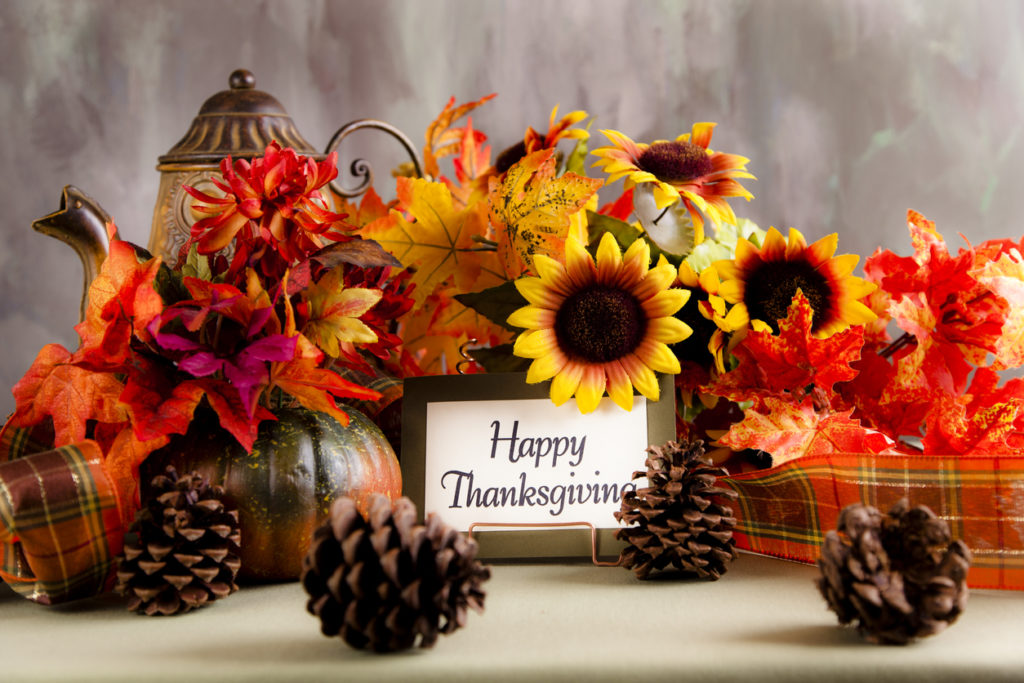 Thanksgiving place setting with autumn floral decorated table. Happy Thanksgiving note card on table with dried floral arrangement centerpieces including leaves, pine cones, and ribbons on dining table.